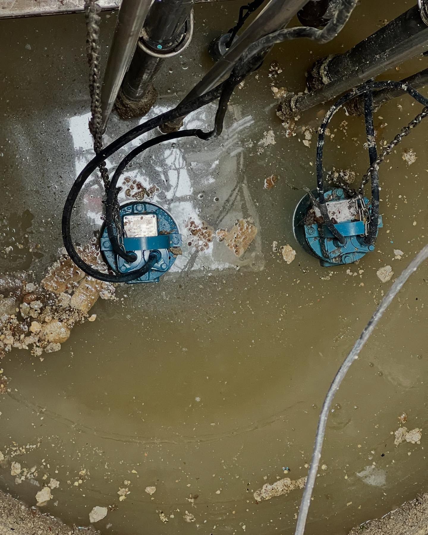 Two submersible pumps sitting in murky water inside a circular basin.