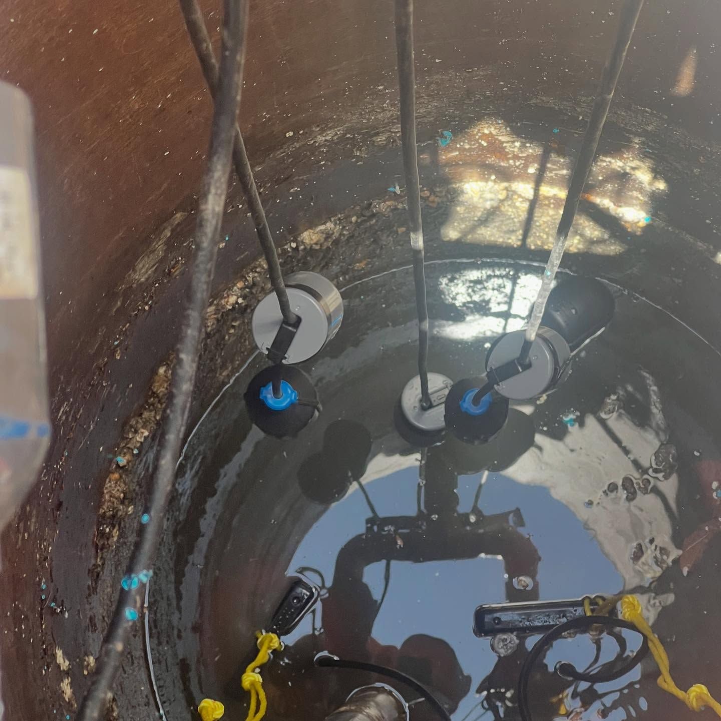 A view inside a dark utility basin showing several submerged, floating float switches attached to black cords.