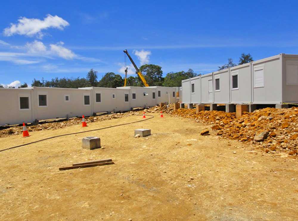 A row of portable buildings are being built in a dirt field.