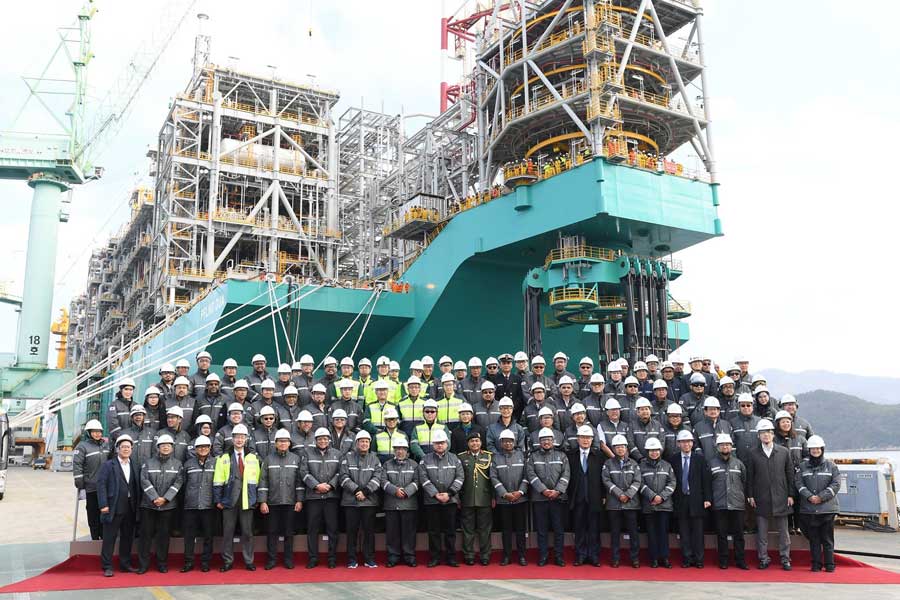 A large group of people are posing for a picture in front of a large ship under construction.