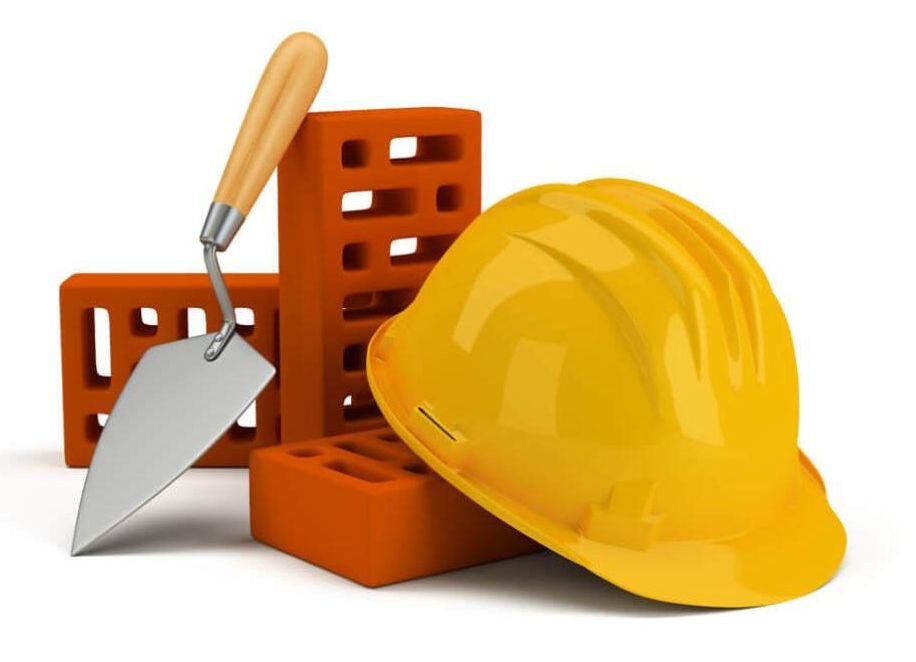 Un casco giallo è appoggiato accanto a una cazzuola e dei mattoni