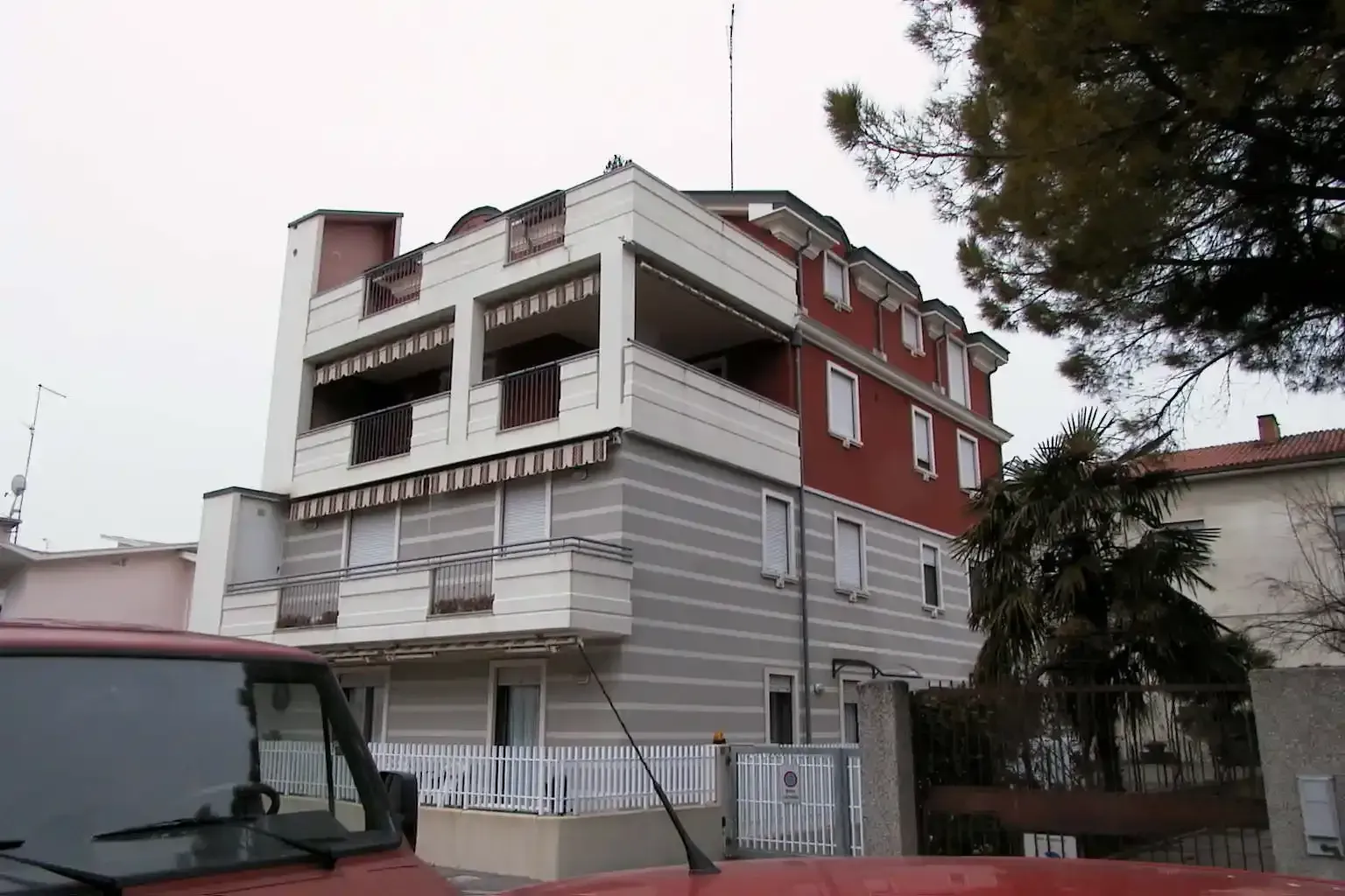 Un edificio residenziale a più piani con i piani inferiori a strisce grigio chiaro e un piano superiore rosso, visto dalla strada.