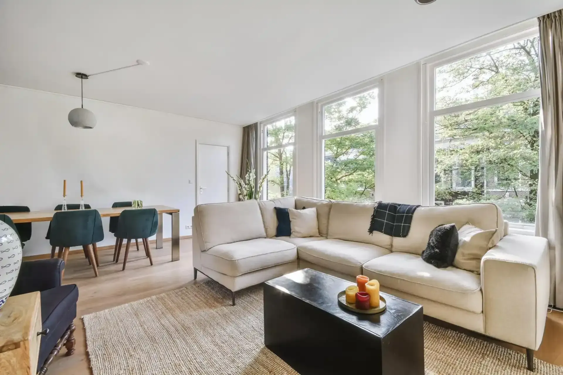 Un soggiorno luminoso con un divano angolare beige, un tavolino da caffè scuro e una zona pranzo con sedie blu.