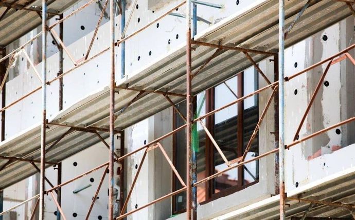 Un edificio in costruzione con pannelli isolanti bianchi sulle pareti esterne, visto attraverso un'impalcatura metallica.
