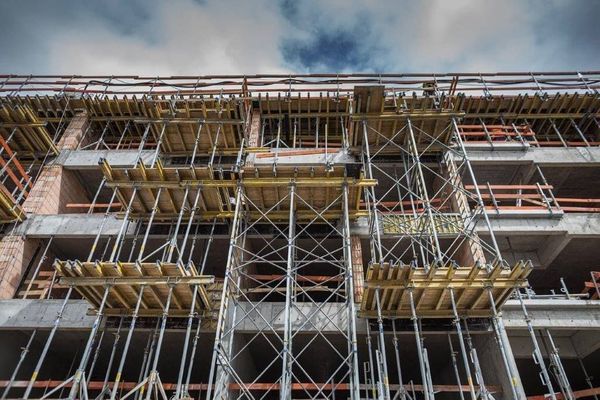 Una ripresa dal basso di un edificio a più piani in costruzione, con pavimenti in cemento a vista e impalcature metalliche.