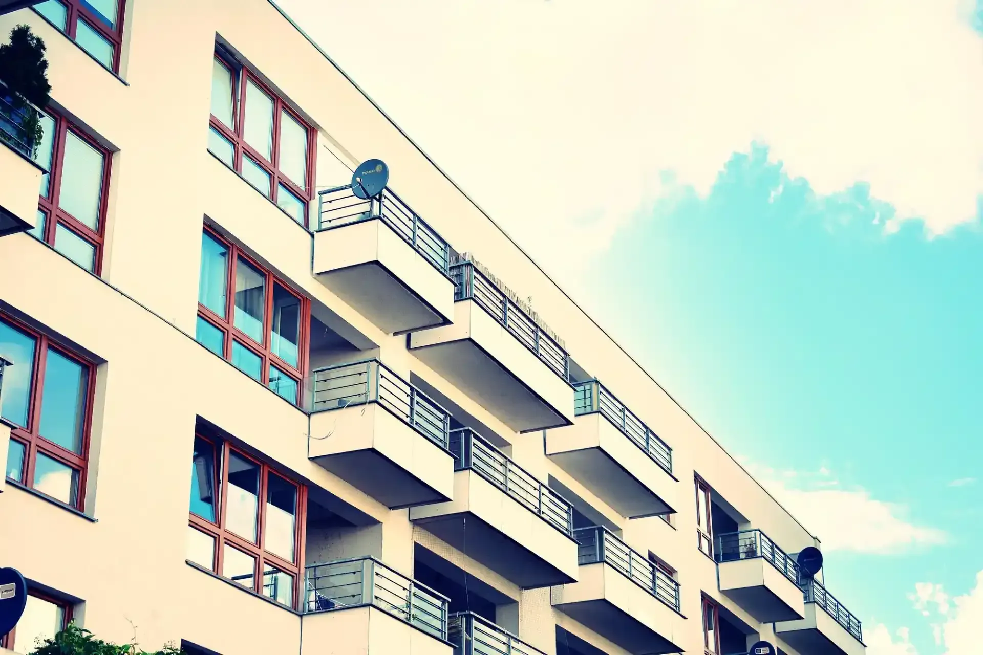 Eine Ansicht aus der Froschperspektive auf ein beigefarbenes Wohnhaus mit Balkonen unter strahlend blauem Himmel.