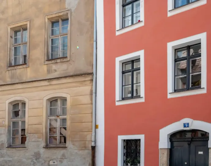 Due edifici adiacenti: uno con una facciata color sabbia, consumata dal tempo, e l'altro appena dipinto di un rosso corallo vibrante e uniforme.