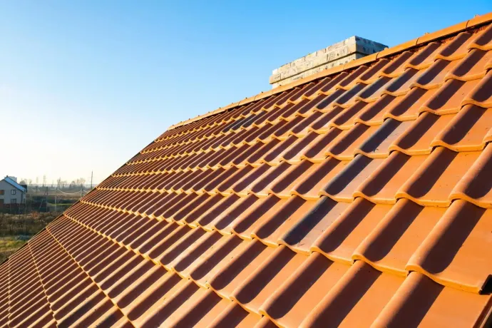 Una vista luminosa e dal basso di un tetto di tegole color terracotta contro un cielo azzurro limpido, con un camino sullo sfondo.