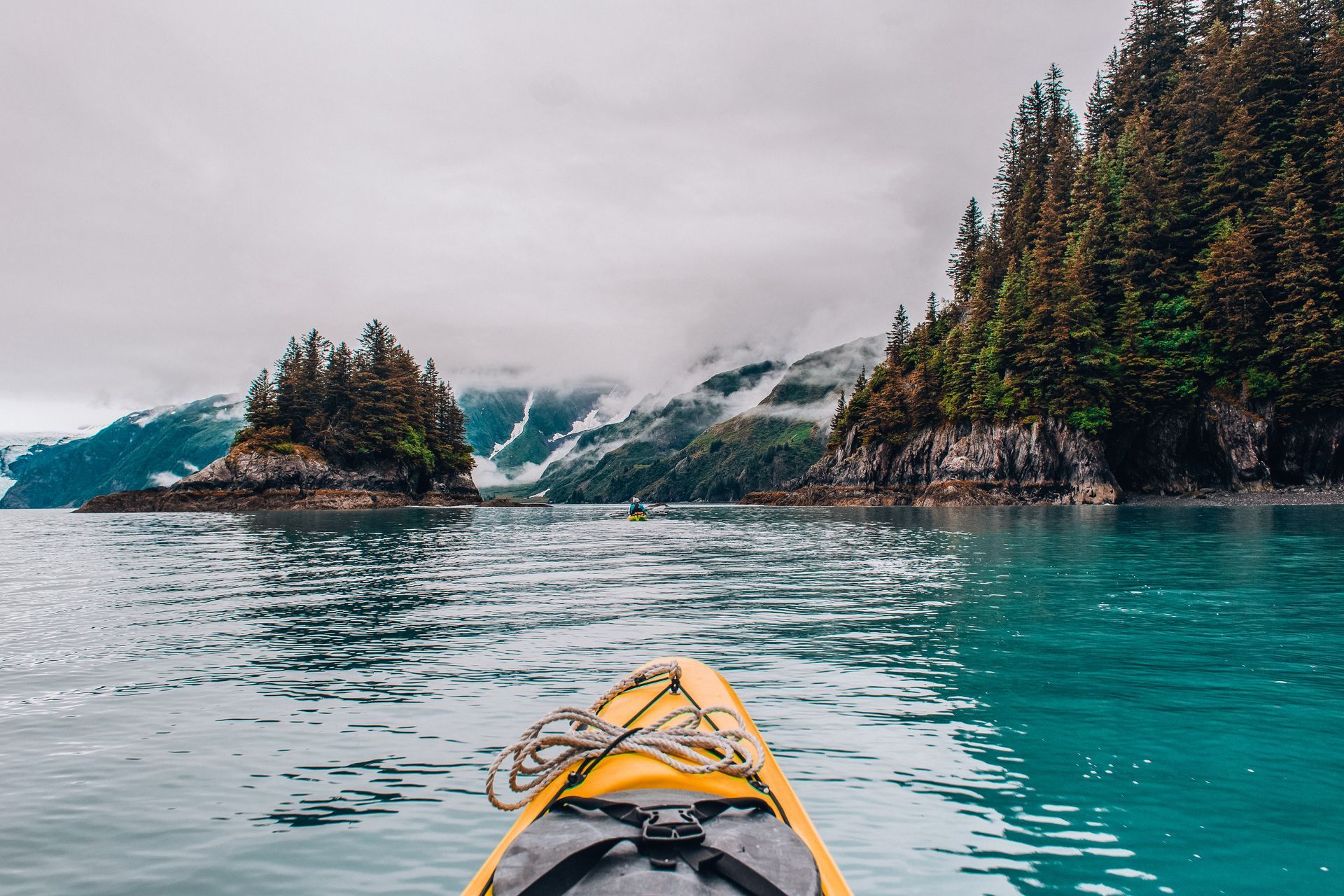 A yellow kayak is floating on a lake with mountains in the background.