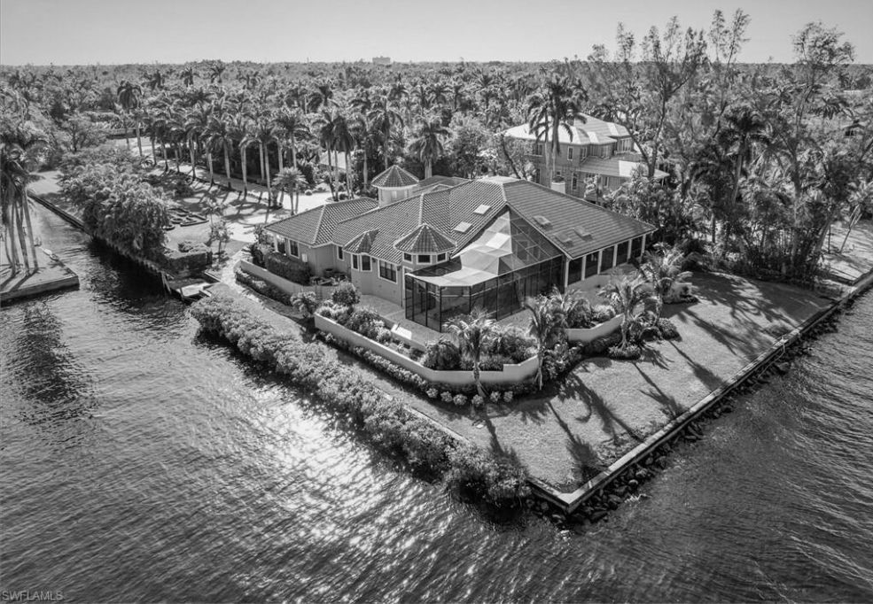 Waterfront home surrounded by water and lush greenery, sunny day.