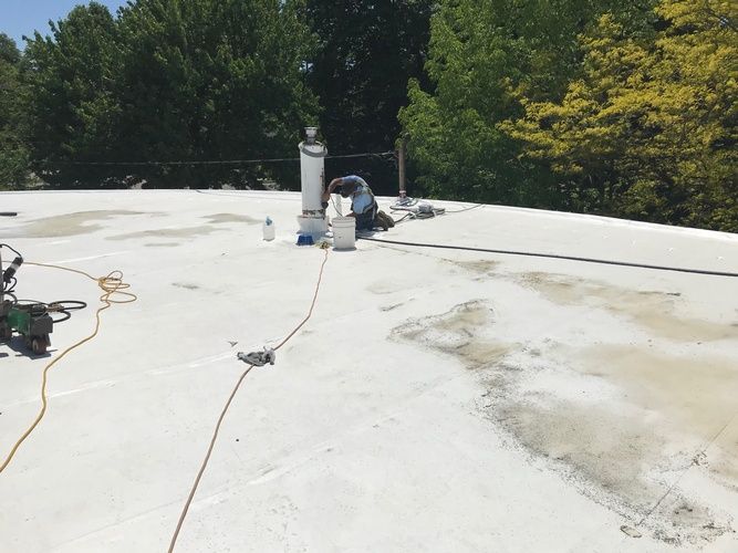 A man is working on a white roof with trees in the background.