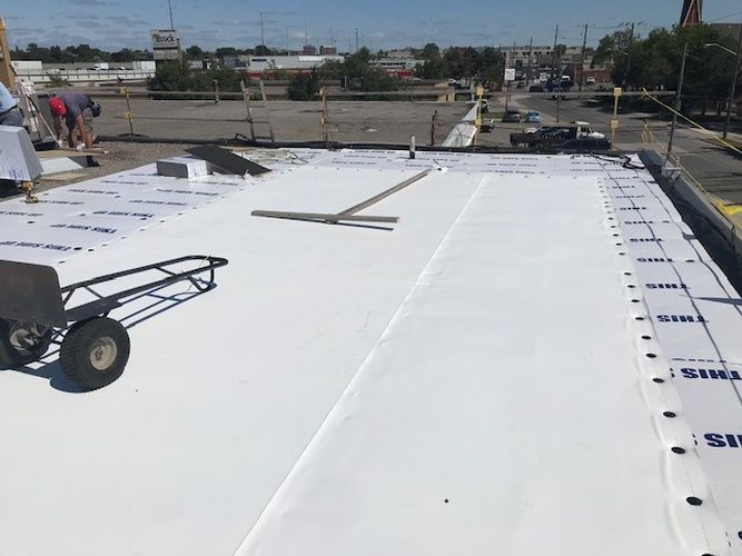A man is working on a white roof with a wheelbarrow.