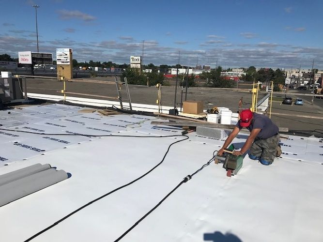 A man is kneeling on top of a white roof.