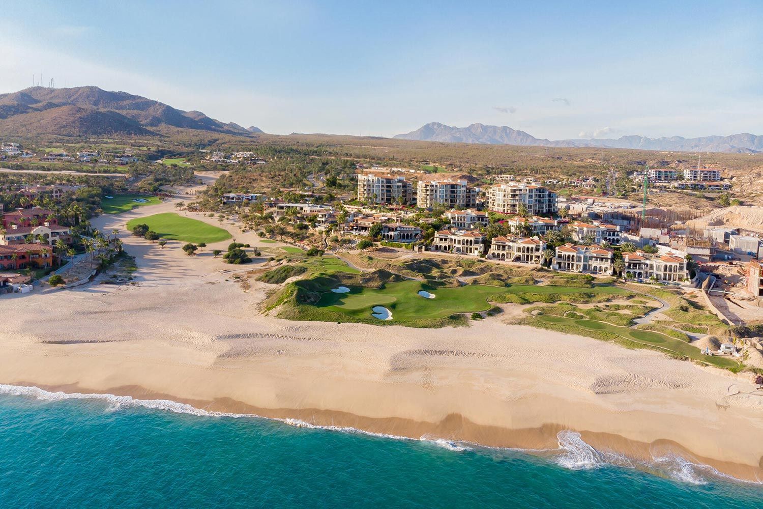 An aerial view of a beach with buildings and mountains in the background.