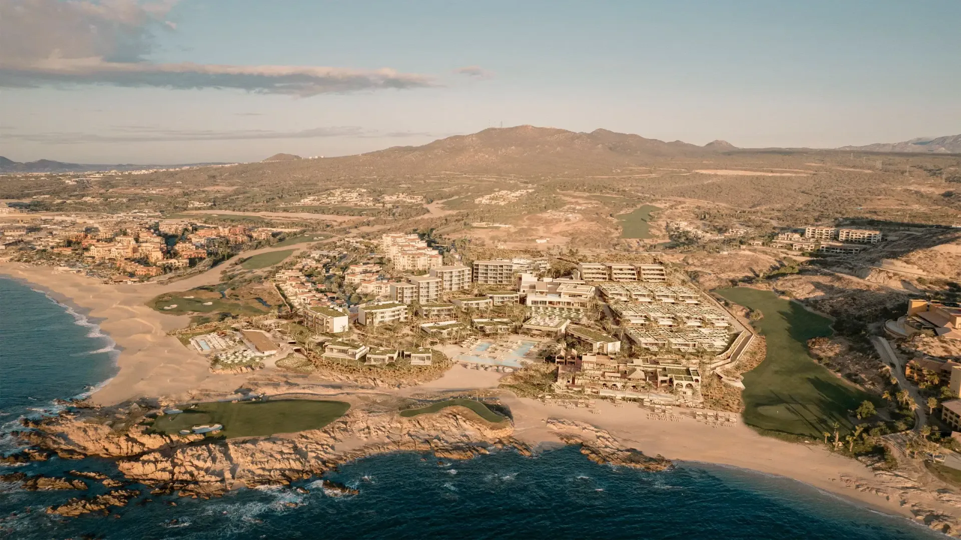 An aerial view of a beach with a golf course and mountains in the background.