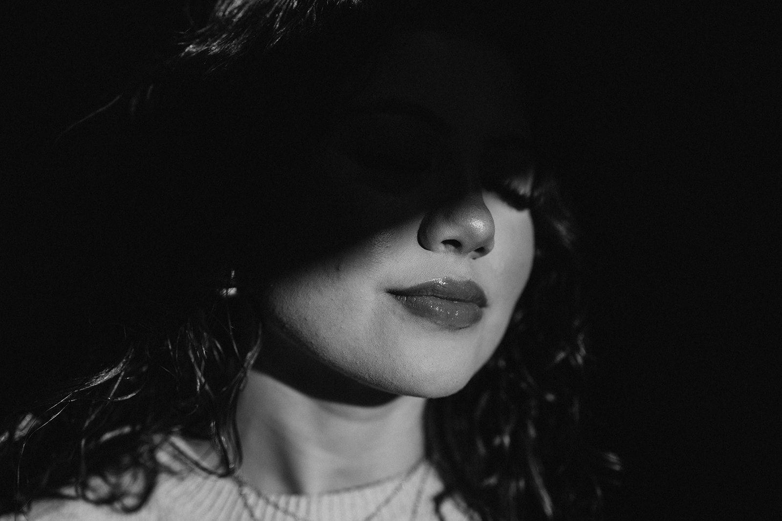 Woman in a white tank top, sitting, hands clasped on knees, legs crossed, on white sheets.