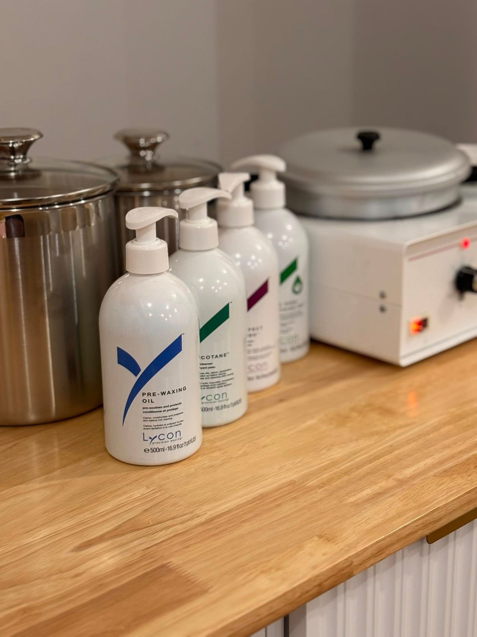 Bottles of lotions lined up on a wooden counter next to wax warmers in a spa setting.