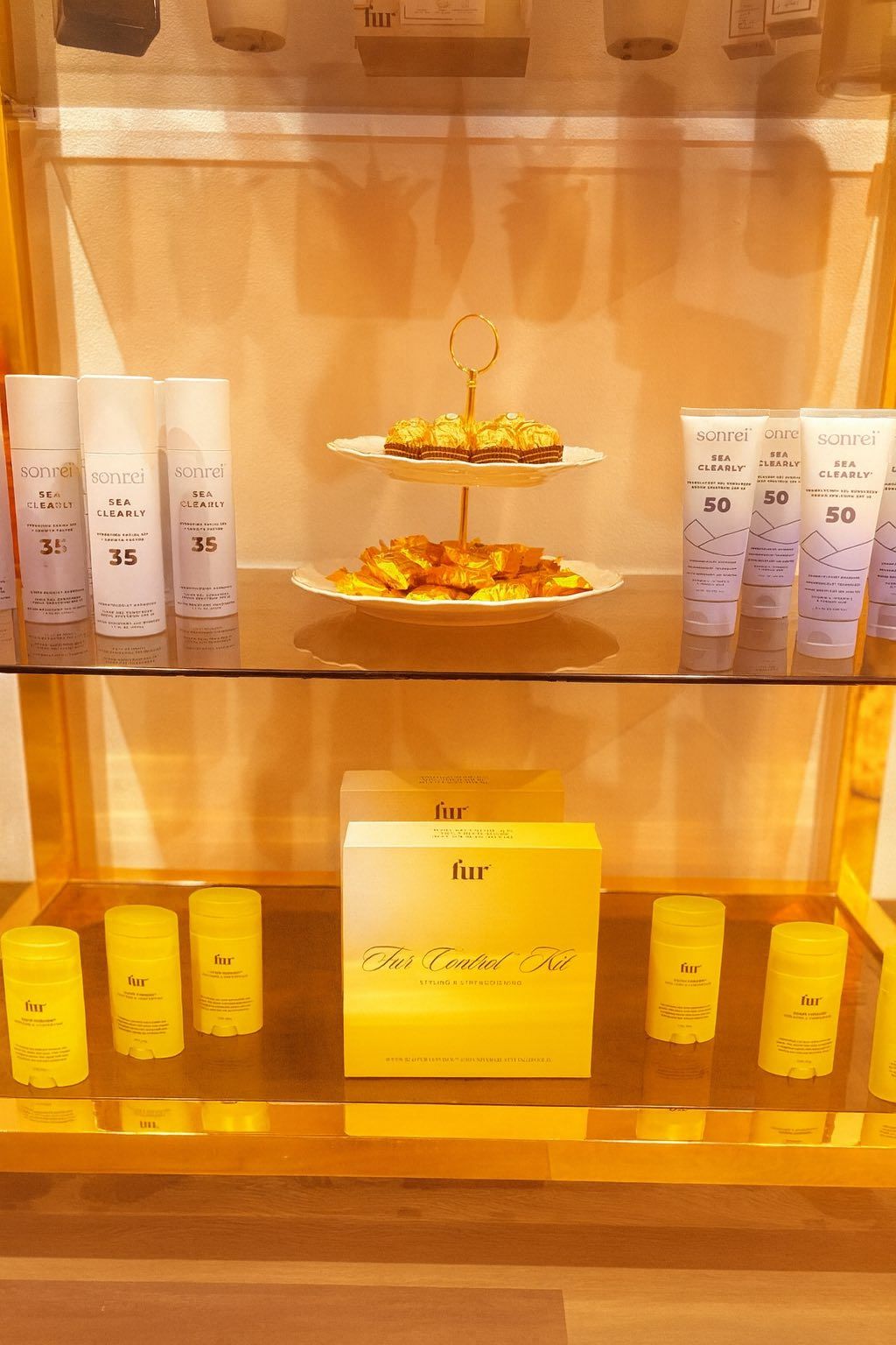 Display case with yellow and white skincare products. A tiered plate of snacks sits in the middle.