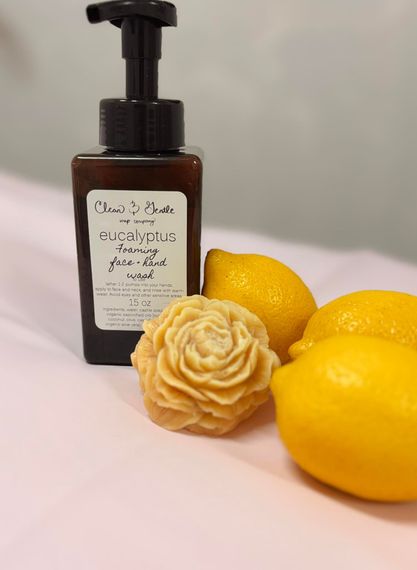 A brown soap dispenser with a label, next to a yellow rose-shaped soap and lemons on pink.