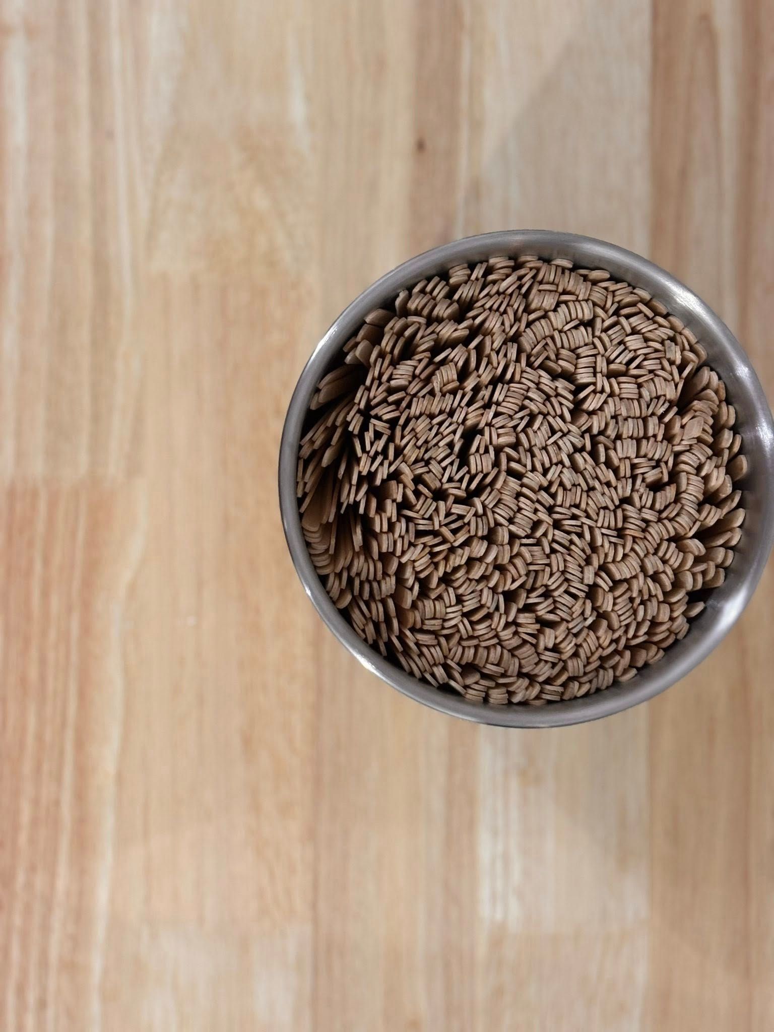 A metal container filled with a mass of brown toothpicks on a light wood surface.