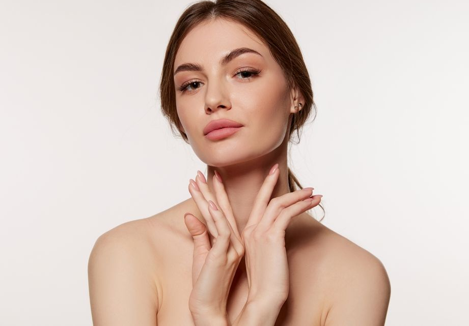 Woman with fair skin, hands near her neck, looking up, soft focus.