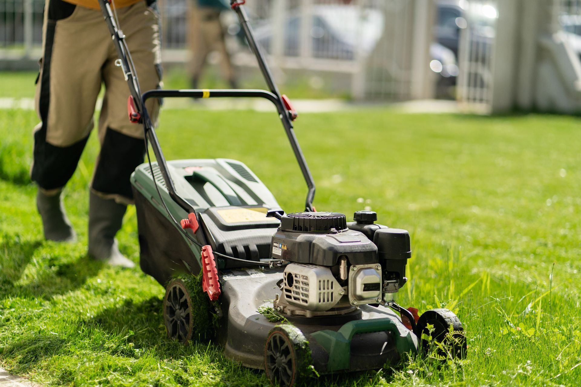 Person mowing a green lawn with a gas-powered lawnmower on a sunny day.