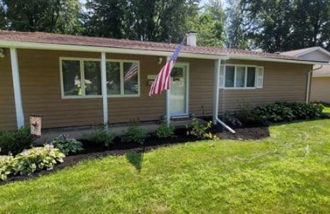 Tan ranch home with American flag, white trim, and landscaped yard.