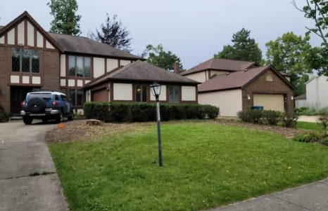 Residential brick houses with a driveway, garage, and green lawn. A blue SUV is parked.