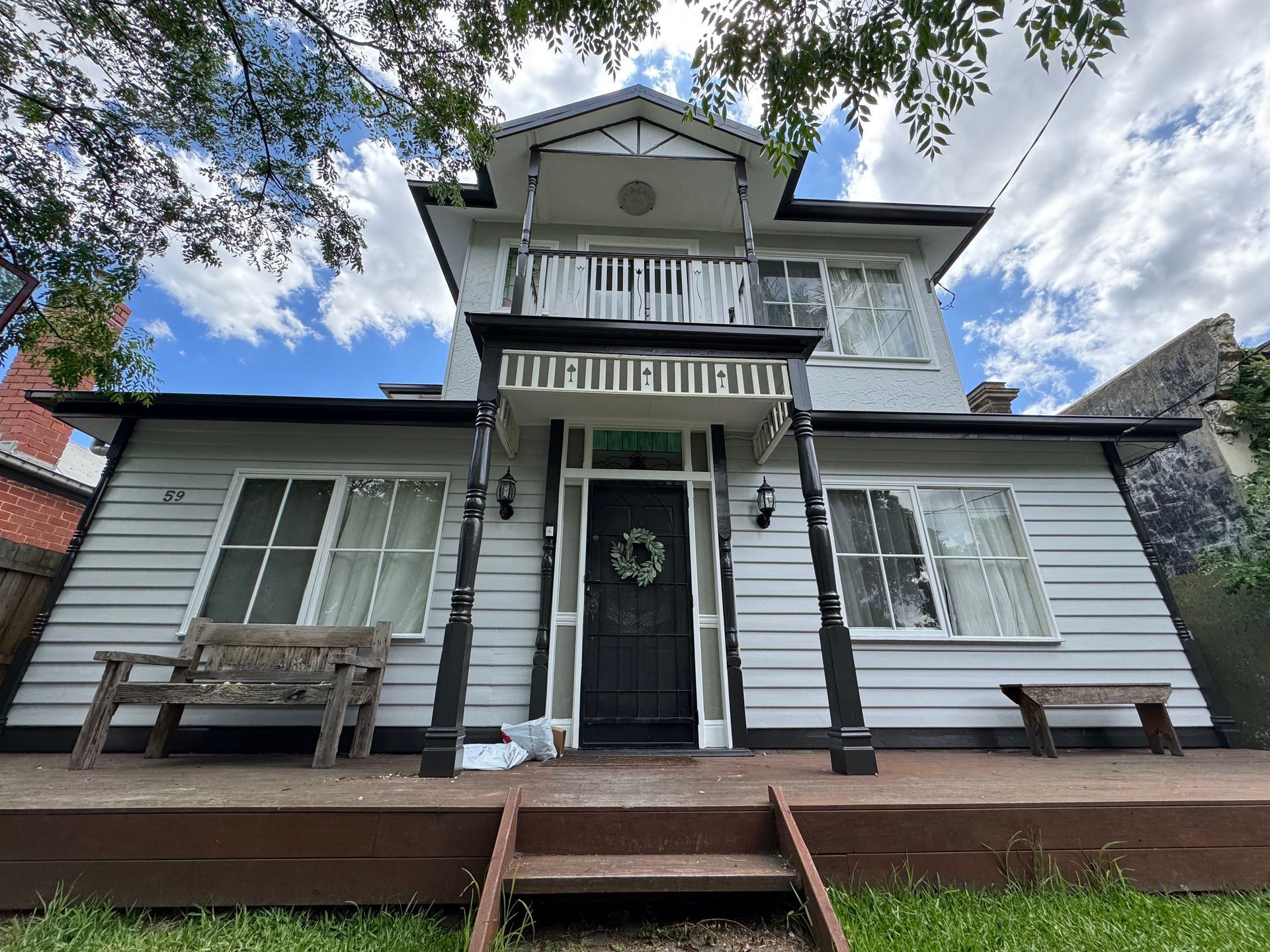 Two-story Victorian house with white siding, black trim, and a small porch. Features a balcony and a front door with a wreath.