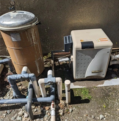 Pool equipment: filter and heater with pipes, set against a concrete wall.