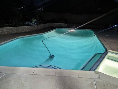 Pool at night with underwater vacuum cleaner running.