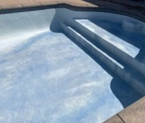 Pool with blue water and steps leading into it. Sunlight reflects on the water's surface.