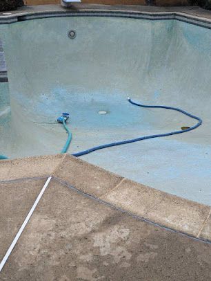 Empty swimming pool with blue hues, hose, and a concrete deck.