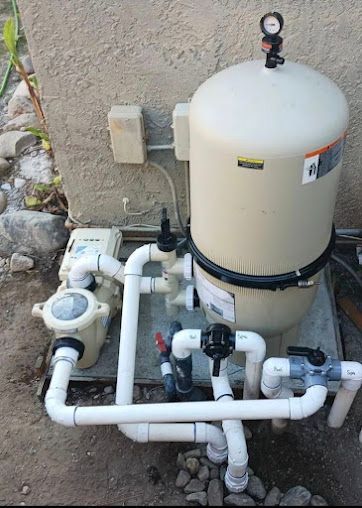 Pool filter system with beige tank, pump, and white PVC pipes against a tan wall.