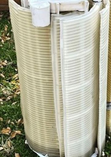 Curved, corrugated plastic window well liners stacked outdoors on grass.