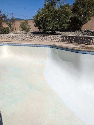 Empty swimming pool with white interior and blue tile trim; stone wall in background.