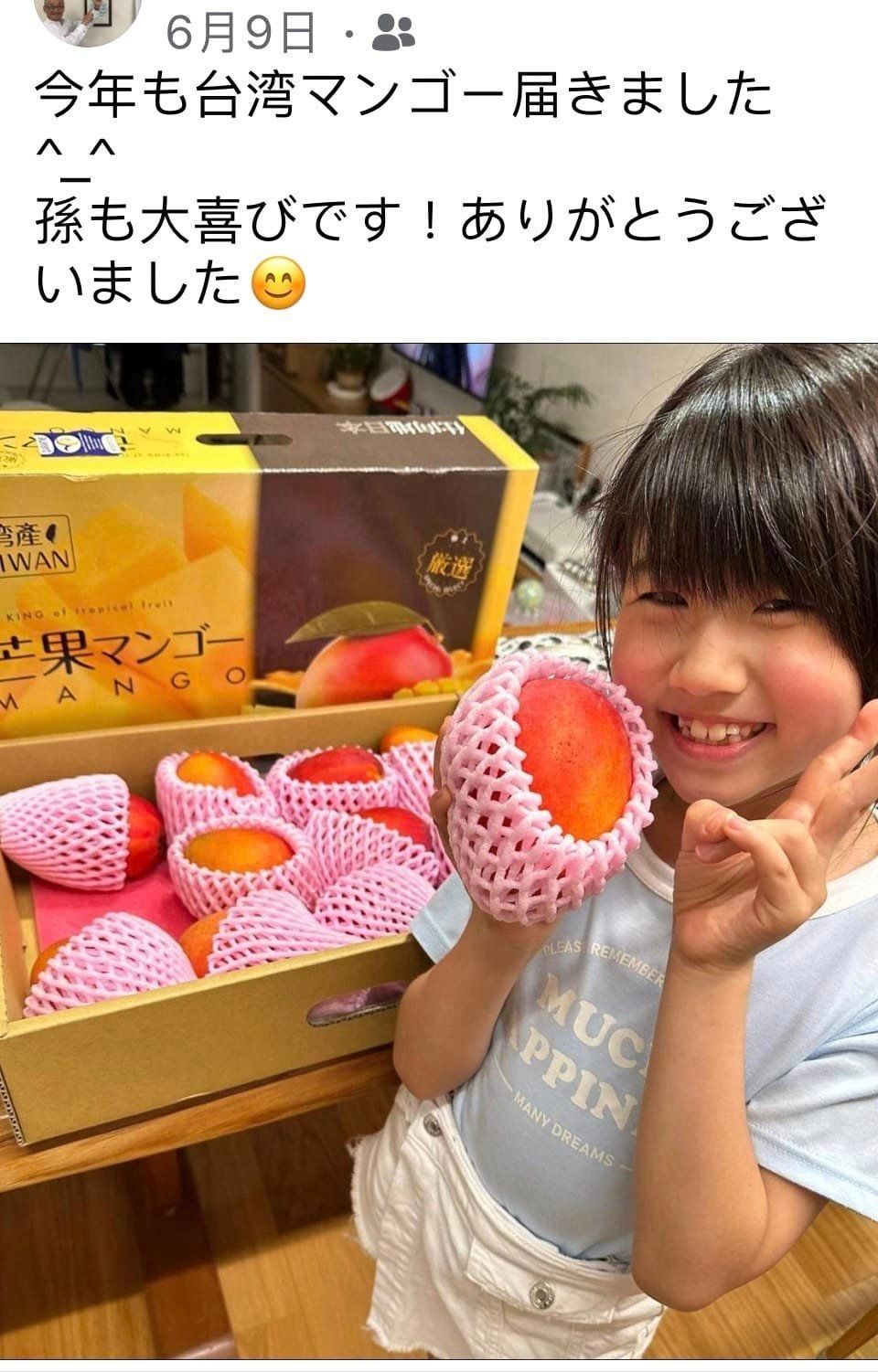 一個小女孩站在一箱芒果前,手裡拿著一顆芒果。