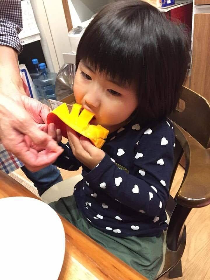 一個小女孩坐在桌邊,嘴裡叼著玩具。