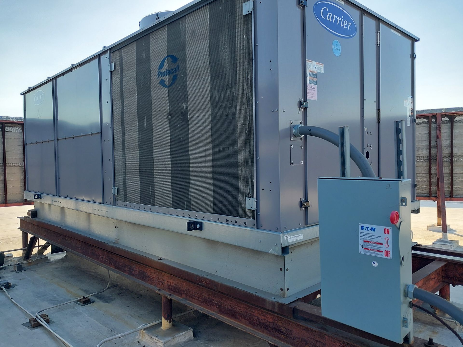 A large industrial air-cooled chiller unit mounted on metal beams on a rooftop under a clear sky.