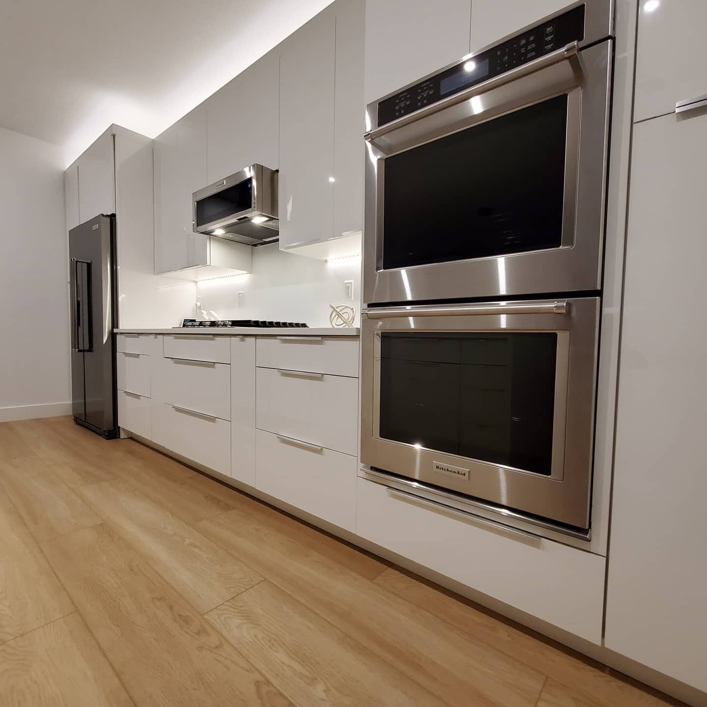 Modern kitchen with white cabinets, stainless steel appliances, and wood flooring.