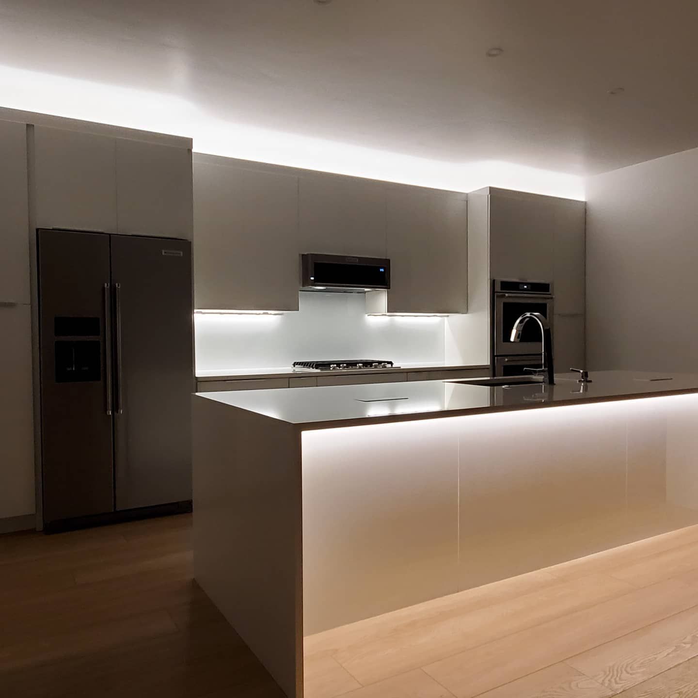 Modern kitchen with white cabinetry, stainless steel appliances, and island with soft lighting.