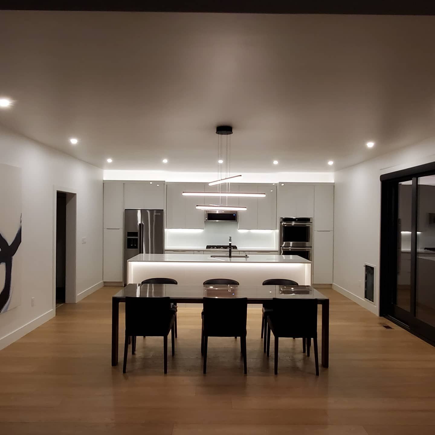 Modern kitchen and dining area with a long black table, four black chairs, and white cabinetry.