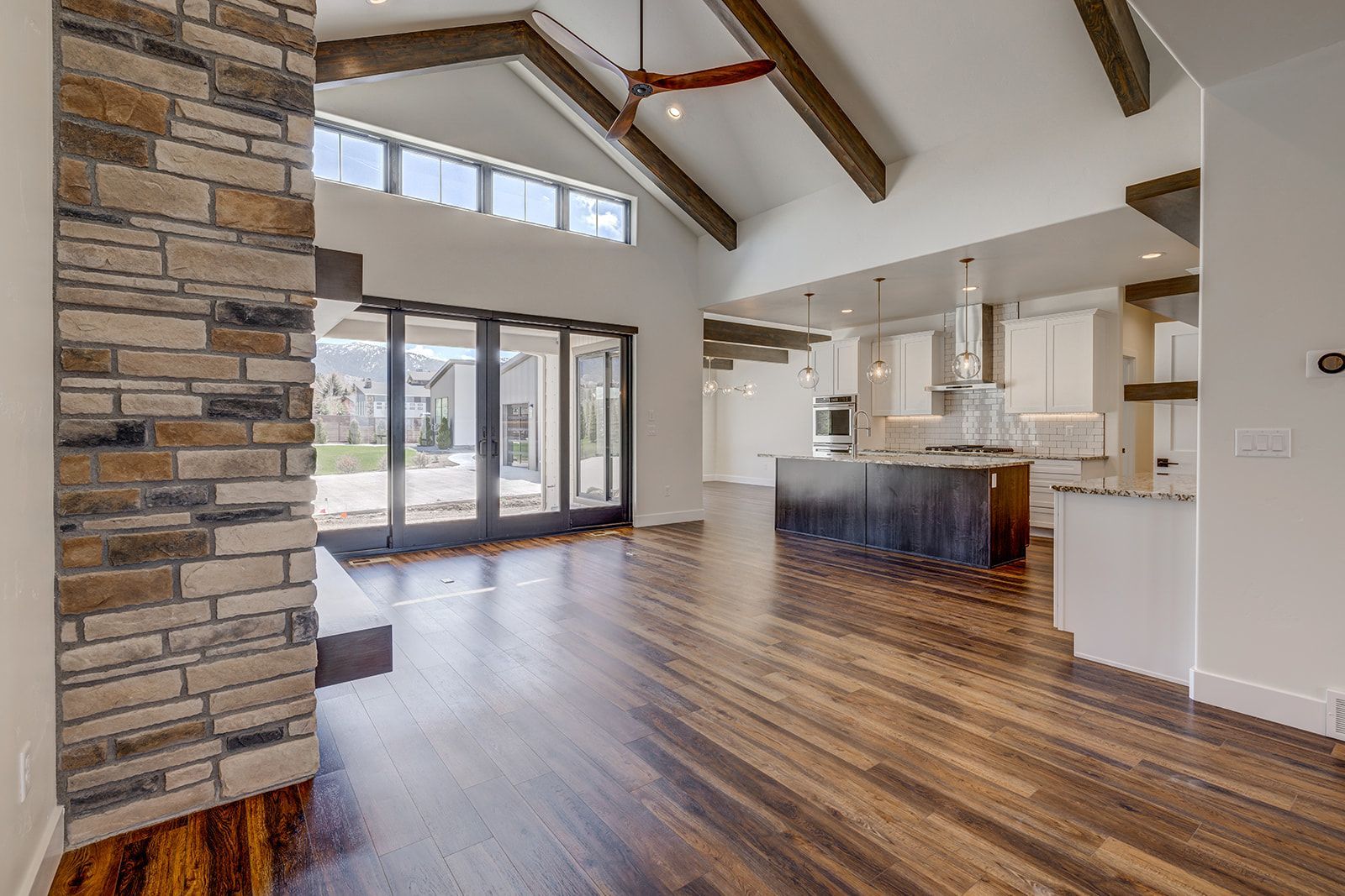 Spacious modern interior with hardwood floors, exposed beams, stone fireplace, and open kitchen.