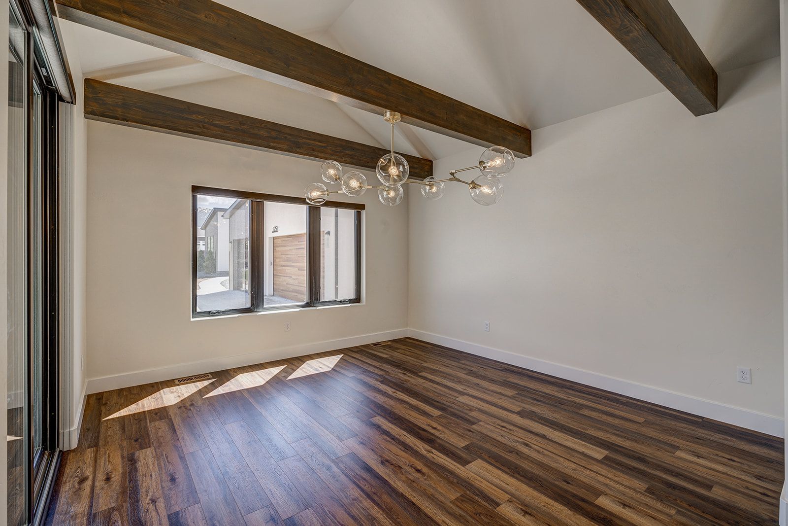 Empty room with wooden floor, white walls, dark beams, and a window.