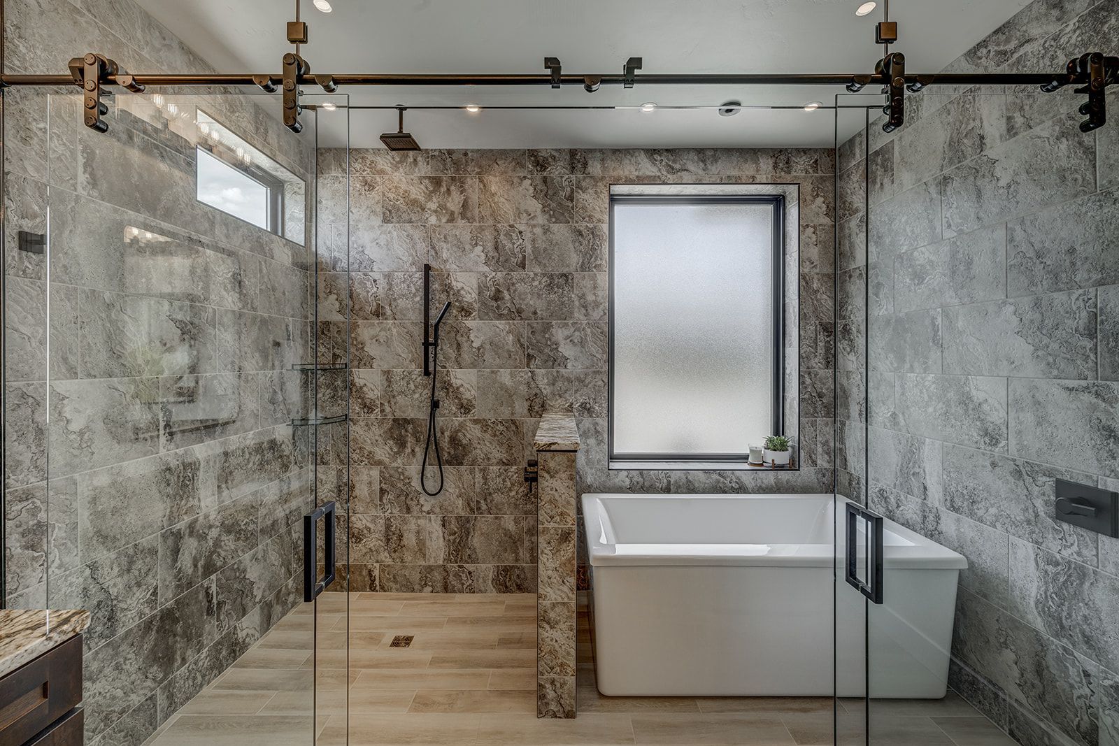 Modern bathroom with gray stone tiles, a glass shower, and a white soaking tub.