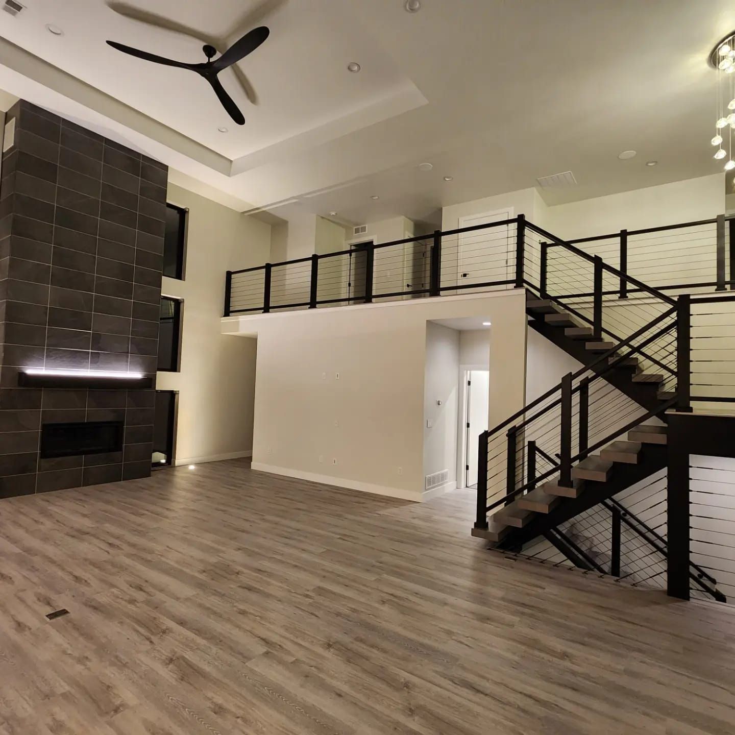 Spacious living room with fireplace, loft, and modern staircase. Neutral colors, hardwood floors, high ceilings.