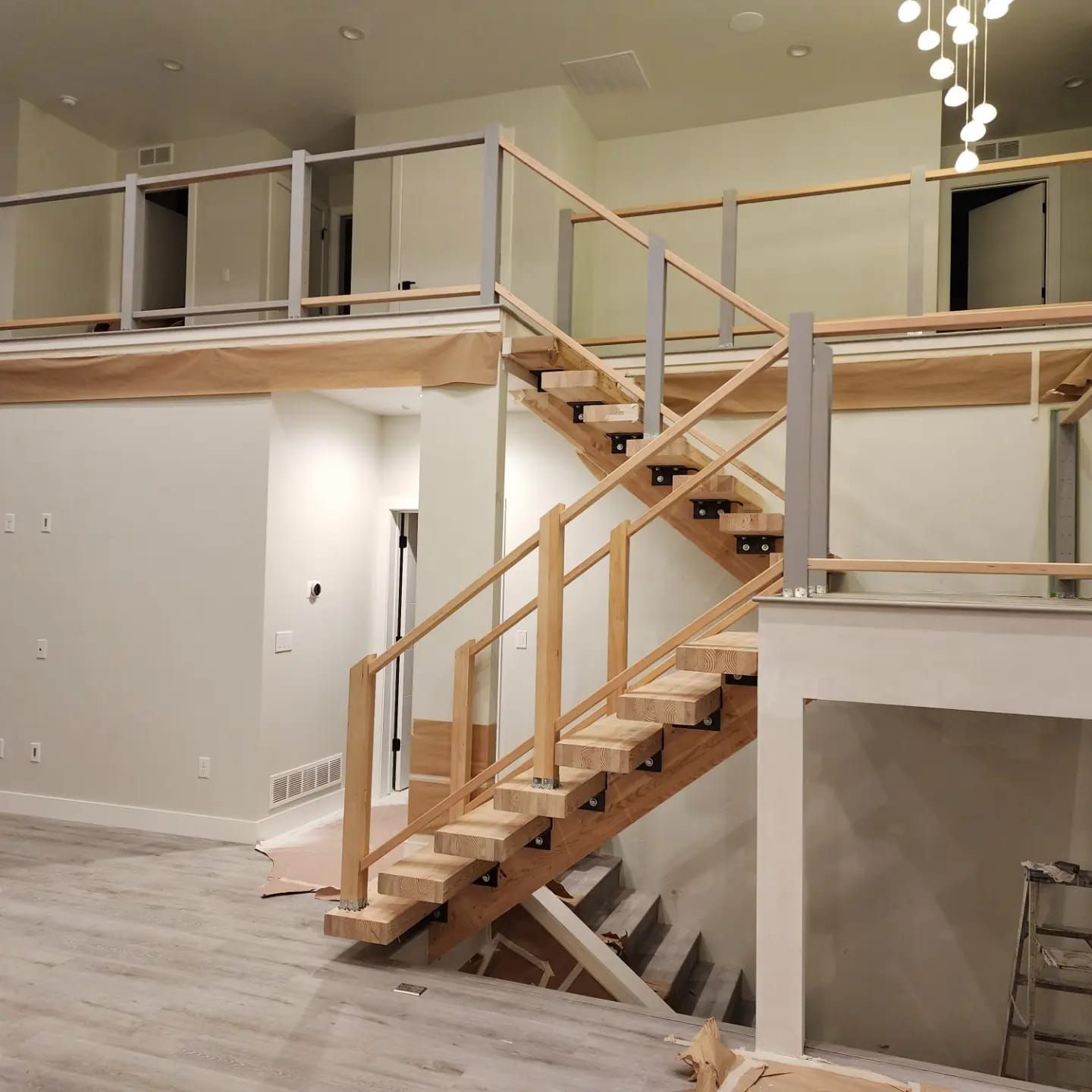 Interior view of a wooden staircase with glass railings and a second-story landing, in a modern home.