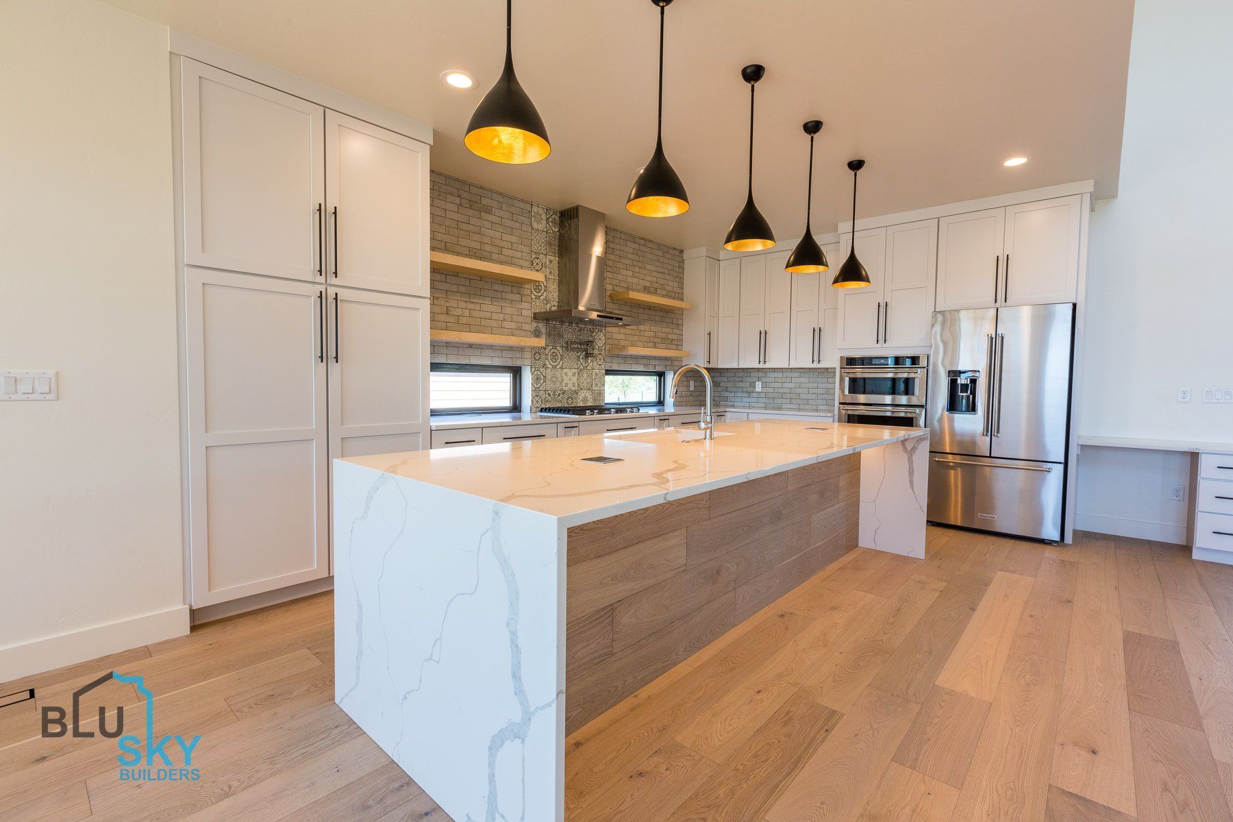 Modern kitchen with white cabinets, island, stainless steel appliances, and wooden floors.