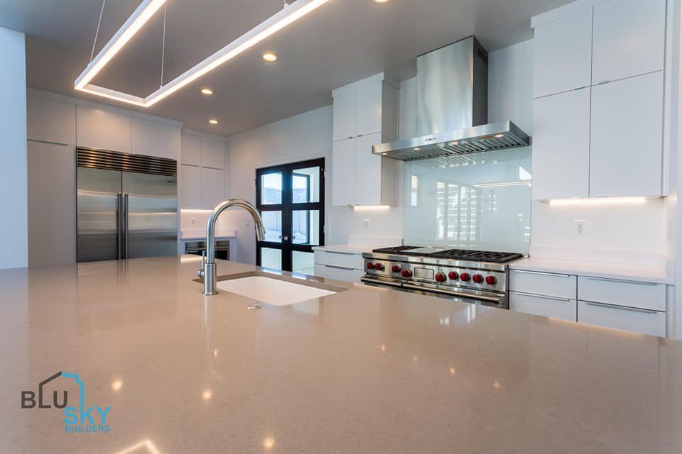 Modern white kitchen with stainless steel appliances, large island, and overhead lighting.