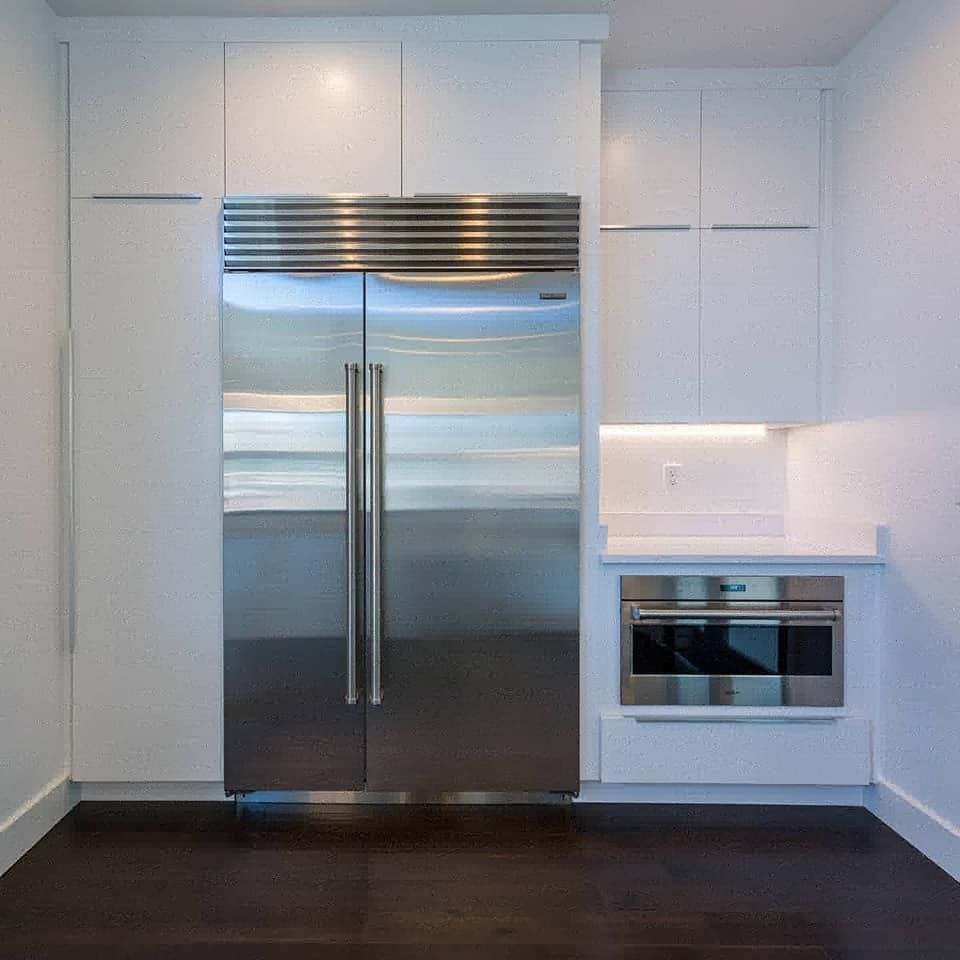 Stainless steel refrigerator flanked by white cabinets and a built-in microwave in a modern kitchen.